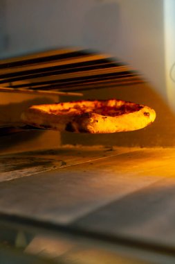 Profesyonel bir mutfakta, pizzacıda siyah giyen genç bir şef spatulayla fırın için çiğ pizza alır.