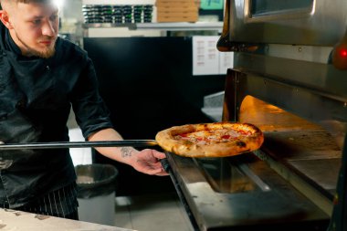 Profesyonel mutfakta, pizzacıda aşçı yeni hazırlanmış pizzayı kürekle tutar.