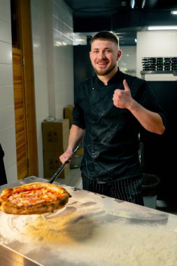 Profesyonel mutfakta, pizzacıda aşçı yeni hazırlanmış pizzayı kürekle tutar.
