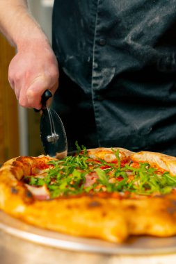 Profesyonel bir mutfakta, pizzacıda, şef pizzayı yuvarlak bir bıçakla parçalara ayırır.