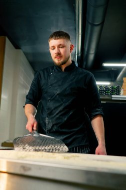 Bir pizzacının profesyonel mutfağında yakın plan çekimde şef masayı un ile sarıyor.