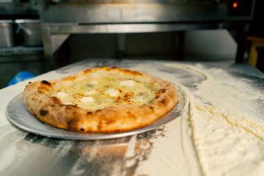 Profesyonel bir mutfağa yakın plan. Masada yeni hazırlanmış pizza var.