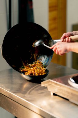 Profesyonel bir mutfağa yakın plan çekimde şef derin bir tabağa sebzeli erişte pişirir ve koyar.