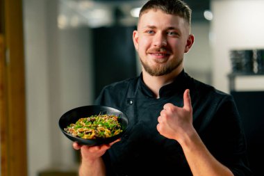 Profesyonel mutfağın yakın plan çekimlerinde şef, pişmiş erişteyle kameraya bakar.