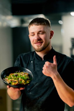 Profesyonel mutfağın yakın plan çekimlerinde şef, pişmiş erişteyle kameraya bakar.