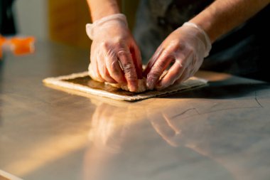 Profesyonel bir mutfakta masanın üstünde eldivenli bir şef suşi topluyor.