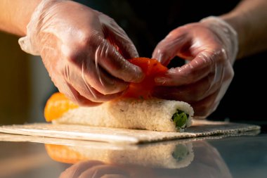 Profesyonel bir mutfakta masanın üstünde eldivenli bir şef suşi topluyor.