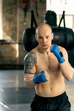 Bir boks kulübüne yakın plan mavi bandajlı kel genç bir boksör gölge boksu profesyonel tekniğini yumrukluyor.