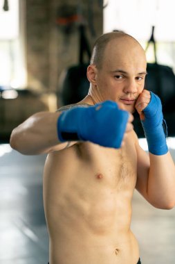 Bir boks kulübüne yakın plan mavi bandajlı kel genç bir boksör gölge boksu profesyonel tekniğini yumrukluyor.