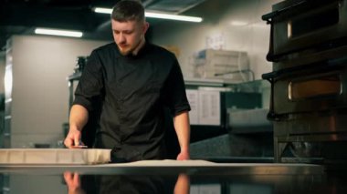 Profesyonel bir mutfakta, pizzacıda siyah üniformalı genç bir şef pizza hamuru hazırlıyor.