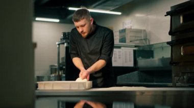 Profesyonel bir mutfakta, pizzacıda siyah üniformalı genç bir şef pizza hamuru hazırlıyor.