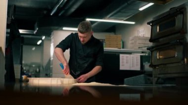 Profesyonel bir mutfakta, pizzacıda siyah üniformalı genç bir şef pizza hamuru hazırlıyor.