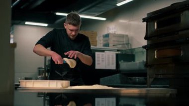 Profesyonel bir mutfakta, pizzacıda siyah üniformalı genç bir şef pizza hamuru hazırlıyor.