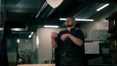 Profesyonel bir mutfakta, pizzacıda, siyah üniformalı genç bir şef havaya hamur krepi fırlatıyor.