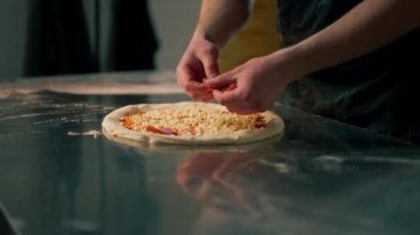 Bir pizzacının profesyonel mutfağında siyah üniformalı genç bir şef pizzanın içine malzeme koyar.