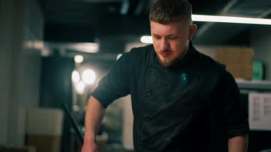 Profesyonel bir mutfakta bir pizzacıda siyahlı genç bir şef spatulayla fırın için çiğ pizza alır.