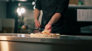 Profesyonel bir mutfakta bir pizzacıda siyahlı genç bir şef spatulayla fırın için çiğ pizza alır.