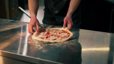 Profesyonel bir mutfakta, pizzacıda siyah giyen genç bir şef spatulayla fırın için çiğ pizza alır.