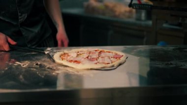 Profesyonel bir mutfakta bir pizzacıda siyah üniformalı genç bir şef fırına pizza koyar.