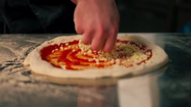 Bir pizzacının profesyonel mutfağında siyah üniformalı genç bir şef pizzanın içine malzeme koyar.