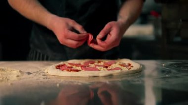 Bir pizzacının profesyonel mutfağında siyah üniformalı genç bir şef pizzanın içine malzeme koyar.
