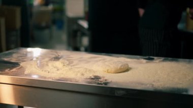 Bir pizzacıda profesyonel bir mutfakta siyah üniformalı genç bir şef pizza hamuru hazırlıyor.