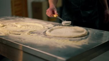 Bir pizzacının profesyonel mutfağında siyah üniformalı genç bir şef pizzanın içine malzeme koyar.
