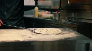 Profesyonel bir mutfakta bir pizzacıda siyah üniformalı genç bir şef fırına pizza koyar.