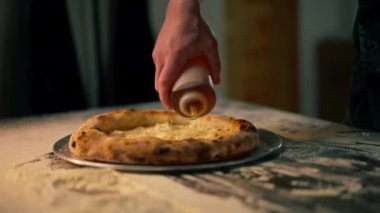 Profesyonel bir mutfakta masanın üzerinde taze hazırlanmış pizza şefin yağı ile servis edilir.