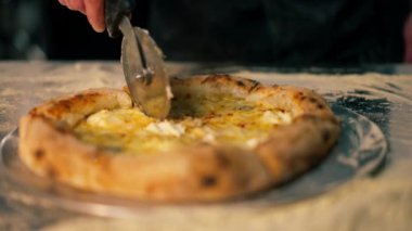Profesyonel bir mutfakta, pizzacıda, şef pizzayı yuvarlak bir bıçakla parçalara ayırır.