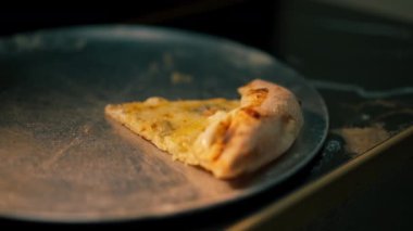 Profesyonel mutfakta şef demir bir tepside uzanır ve yanında peynirli bir üçgen pizza olur.