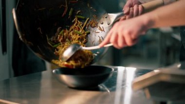 Profesyonel bir mutfağa yakın plan çekimde şef derin bir tabağa sebzeli erişte pişirir ve koyar.