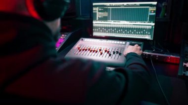 Kayıt odasının karanlığında stüdyoda neon ışıkla birlikte ses mühendisi konsolda çalışır sesi ayarlar ve sesi karıştırır.