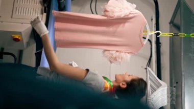 dikey video profesyonel kuru temizlemeci genç kız buharlı bir askıda pembe bir kazak ütülüyor.