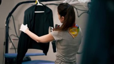 Profesyonel kuru temizlemeci kız siyah bir kazağı buharlı bir askıda ütülüyor.