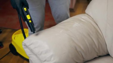Bir dairede profesyonel temizliği kapatmak. Temizlikçi yıkamadan önce tekstil kanepesini ıslatır.