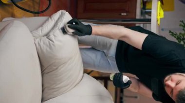 Dikey video profesyonel temizlik. Bir temizlikçi deri kanepeyi cilalıyor.