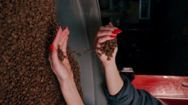 Kızartma fabrikasında çekilen dikey videoda bir kız elinde taze kavrulmuş kahveyi yudumluyor.