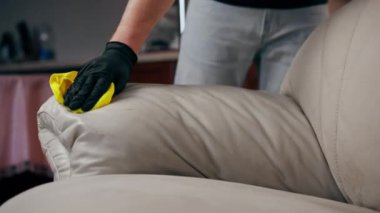 Bir apartman dairesinde profesyonel temizlik kapanıyor. Temizlikçi, cilalama ajansını deri kanepeye uyguluyor.