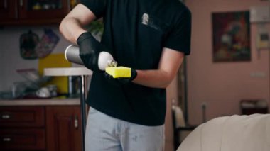 Bir apartman dairesinde profesyonel temizlik kapanıyor. Temizlikçi, cilalama ajansını deri kanepeye uyguluyor.