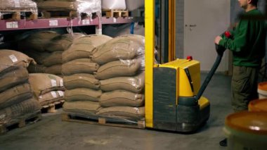 Bir kahve fabrikasındaki işçinin paleti indirmek için sarı bir forklift kullandığı yakın plan.