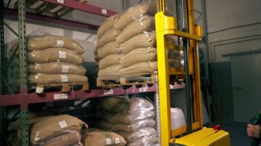 Kahve fabrikasında çalışan bir işçi sarı bir forklift kullanır ve rafa bir palet koyar.