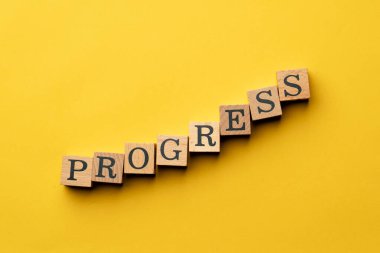 Gölgeler olmadan sarı, sıcak arka plan. Siyah harfli tahta küpler kelime ilerlemesini ortaya koyuyor.