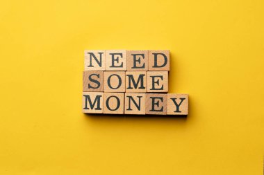 Gölgeler olmadan sarı, sıcak bir arka plan. Siyah harflerle yazılmış tahta küpler. Biraz paraya ihtiyacım var.