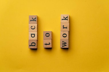 Gölgeler olmadan sarı, sıcak bir arka plan. Siyah harfli tahtadan küpler işe geri dönüyor.