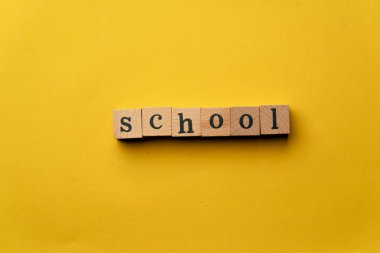 Gölgeler olmadan sarı, sıcak bir arka plan. Siyah harflerle yazılmış tahta küpler. Kelime okulu.