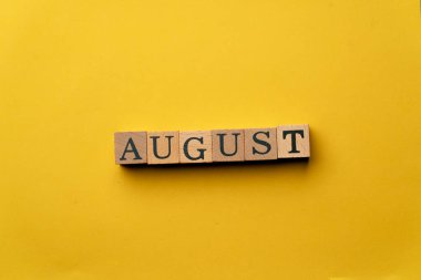 Gölgeler olmadan sarı, sıcak bir arka plan. Siyah harfli tahta küpler. Ağustosta yayılmış.