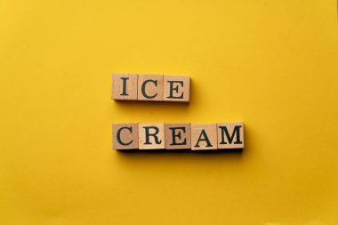 Gölgeleri olmayan sarı, sıcak bir arka plan. Siyah harfli tahta küpler. Dondurma serpiştirilmiş.