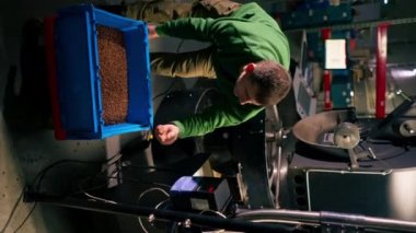 Dikey videoda kahve kızartan bir fabrika işçisi mavi bir kahve kutusu açar ve makineyi çalıştırır.