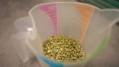 Üzerinde yeşil kahve olan bir ölçü kabının içindeki bir masanın üstündeki kızartma fabrikasının en üst görüntüsü.